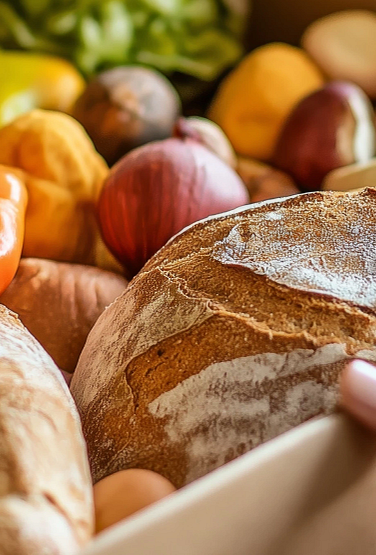 In a heartfelt act of giving, hands are shown passing a Thanksgiving meal box overflowing with fresh vegetables, bread, and canned goods